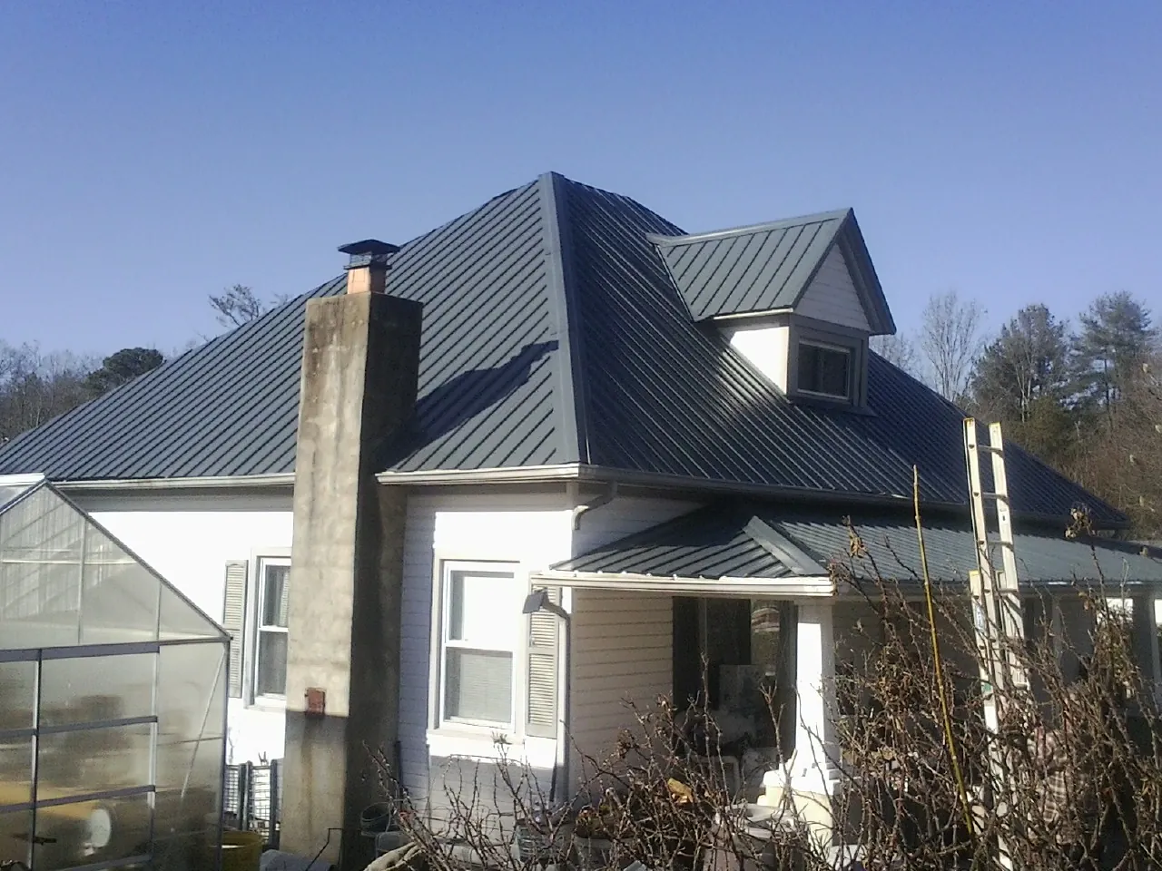 Dark blue standing seam metal roof on a white farmhouse with dormer — Slate & Tile Roof Repair by Roofing Brothers in North Port