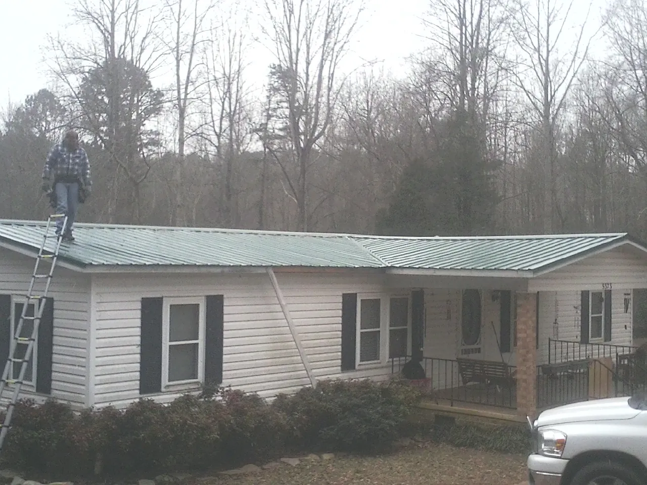Worker on a ladder beside a new green metal roof on a ranch home in North Port