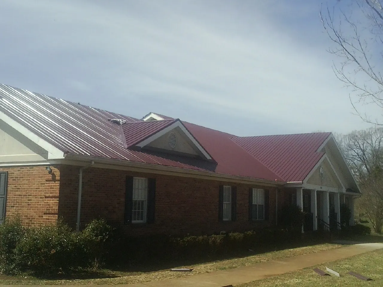 Red metal roof with gabled entries on a long brick building, from a Hail Damage Roof Repair job in North Port
