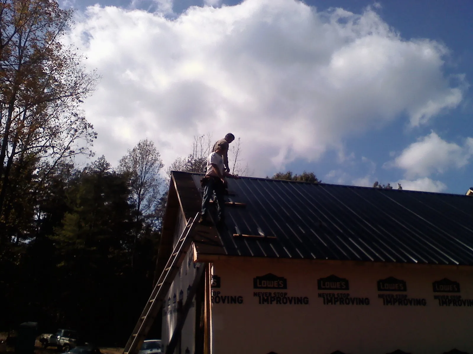 Roofer fastening dark metal panels high against a cloudy sky, from a Roof Inspection job in North Port