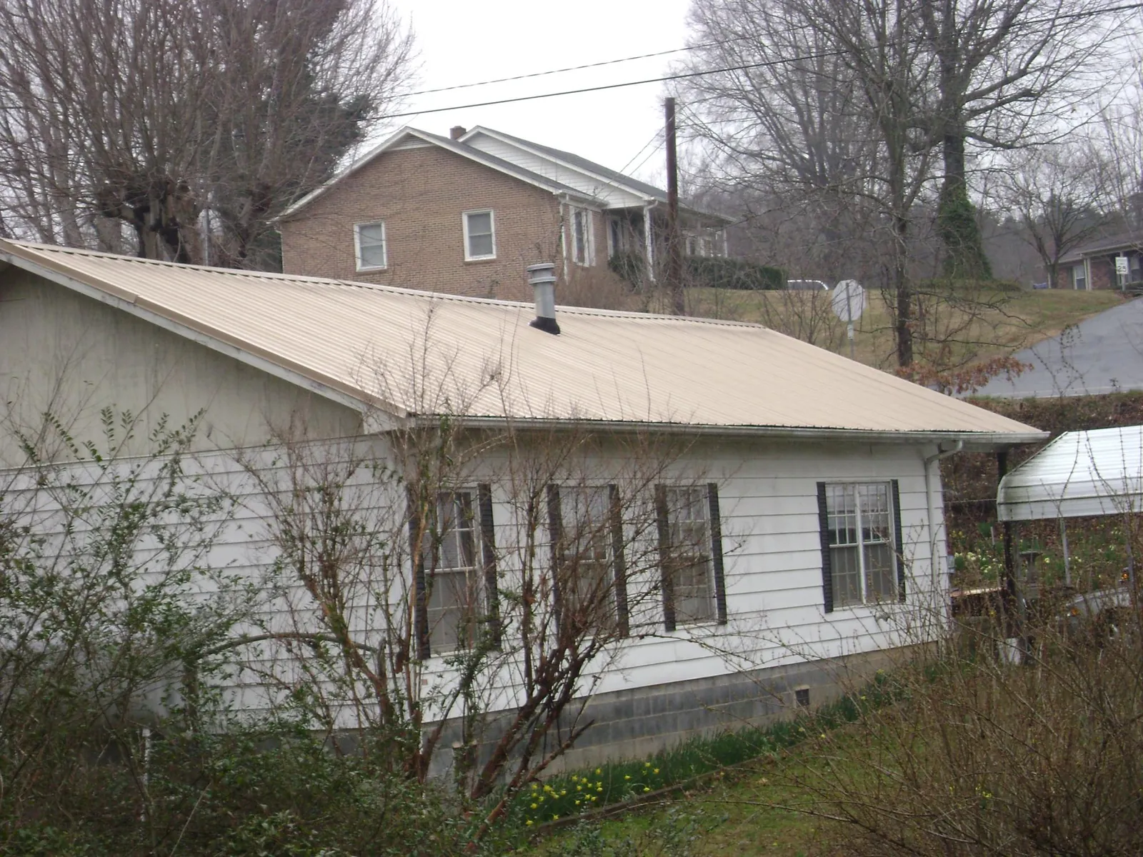 Tan metal roof on a white sided house set into a hillside — Commercial Roofing by Roofing Brothers in North Port